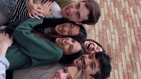 Happy group of young students hugging each other laughing outdoors. Friendly group of millennial friends having fun together at city street. Vertical video.