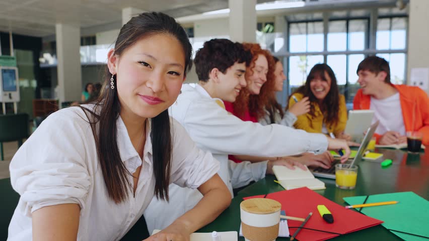 Millennial student girl smile at camera with young people at campus college. Portrait of asian woman sitting at table with classmate friends working together on school project. 