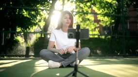 Blogger recording video at sports field Using smartphone outdoor. Beautiful young woman blogger broadcasts live on a social network. The girl is blogging, reviewing products