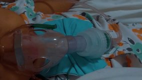 Little girl inhaling medical nebulizer in hospital bed. with angle video closeup of the face