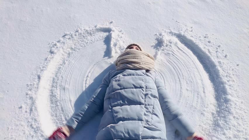 Young woman making a snow angel playing in snow on sunny winter day