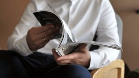 a businessman in a white shirt sitting in a chair leafing through a fashionable business magazine.slow video