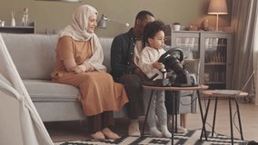 Slowmo of cute 3 year old boy playing race video game on laptop using gaming steering wheel, spending time with interracial Muslim parents at home