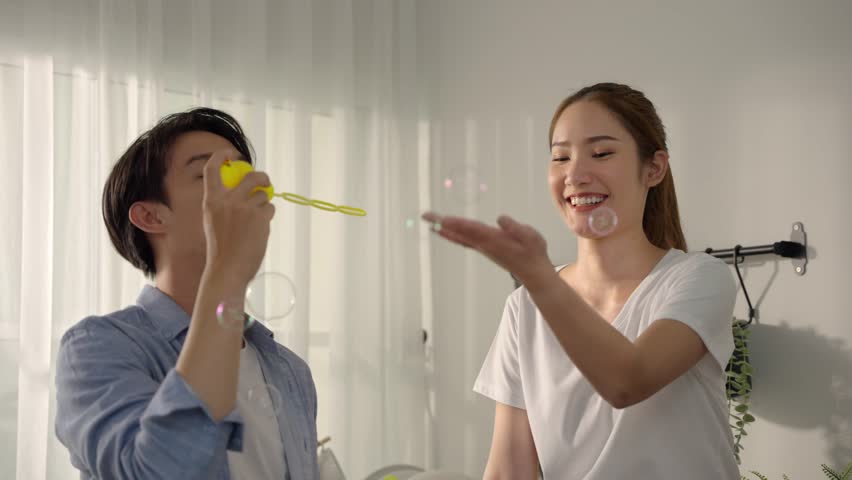 Happy couple having great time in Kitchen, In their cozy home kitchen, a playful Asian couple finds pure joy, blowing bubbles and creating cherished memories with genuine smiles and carefree spirits