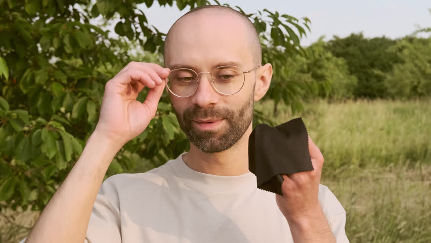 closeup young charismatic man wipes gold-rimmed glasses with napkin, checks cleanliness and transparency of lenses, concept of eyewear maintenance, optical care, lens hygiene, eyeglass longevity