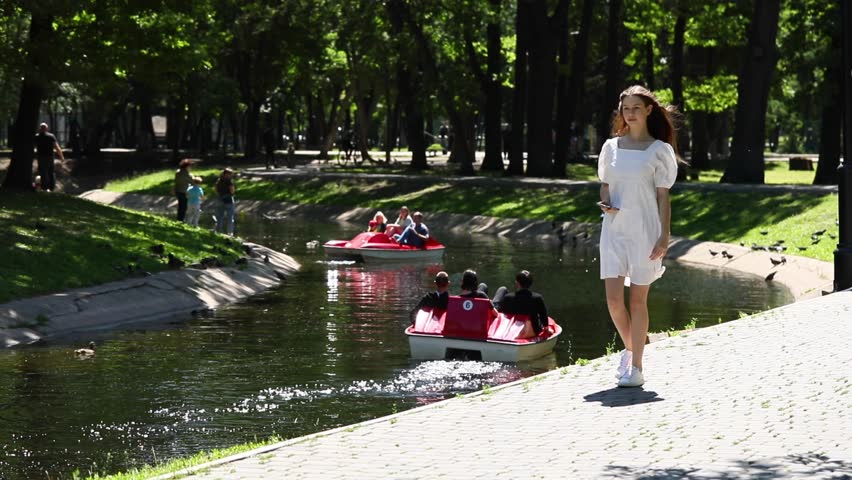 Young beautiful girl in a white dress walks in a summer park
