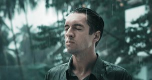 Portrait of a pensive man closed his eyes and stands in the rain. Cinematic video pensive man thinking and getting wet under heavy summer rain outdoors. Rain season