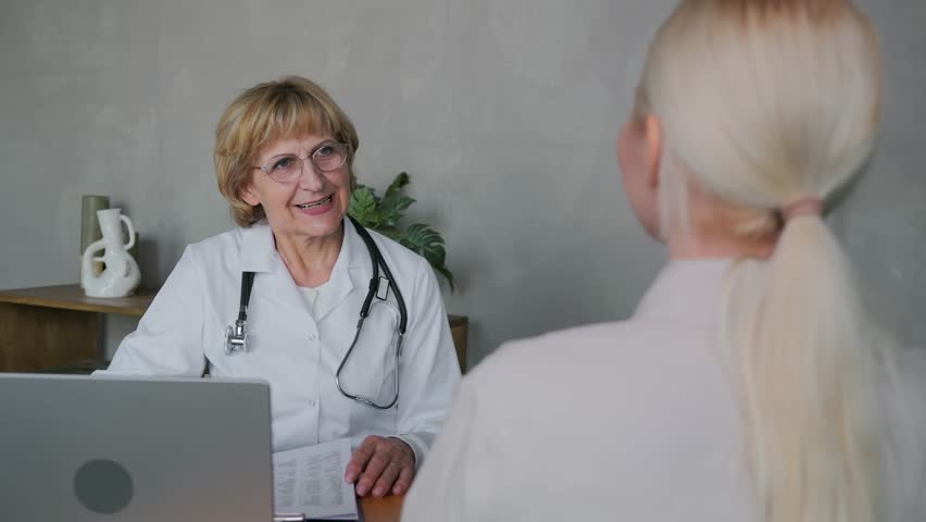 A positive elderly woman general practitioner doctor with a smile communicates with a female patient in her office and announces excellent good examination results. High quality 4k footage Royalty-Free Stock Footage #1105171467