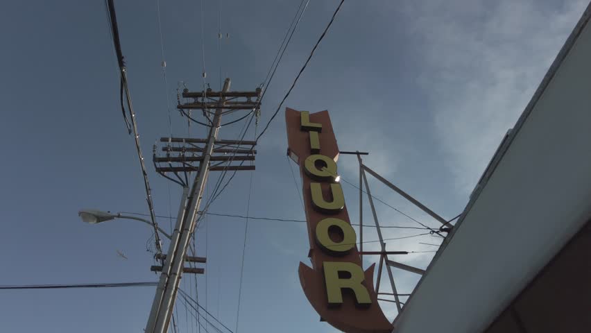 Liquor Store Arrow Sign with Blue Skies Electricity Poles and Airplane Flying By