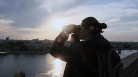 A young female tourist looks through binoculars, exploring the city and the Danube river at sunset. Silhouette of a hipster woman while an evening walk on the river embankment. - Powered by Shutterstock - Get 15% off with code: PIKWIZARD15