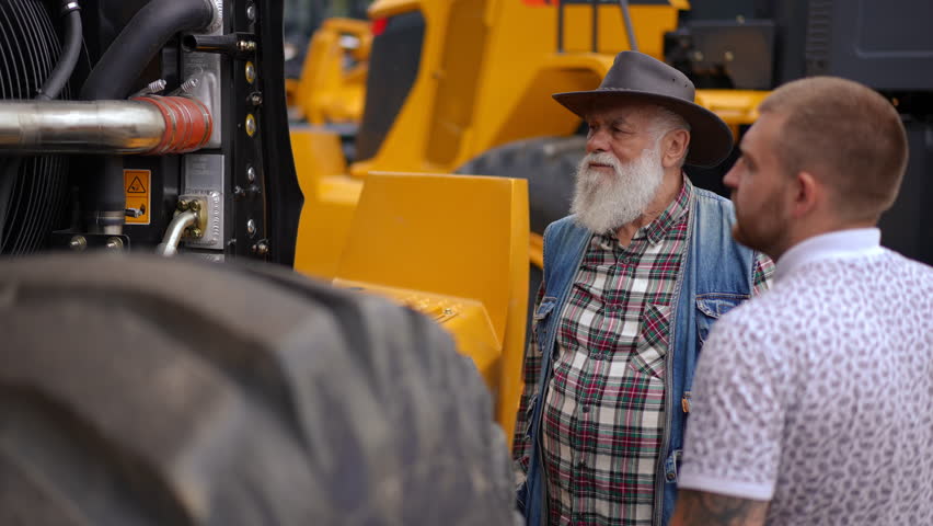 Portrait of concentrated senior man choosing new tractor talking with young guy advertising vehicle. Bearded Caucasian farmer buying harvester chatting with seller in slow motion Royalty-Free Stock Footage #1105183977