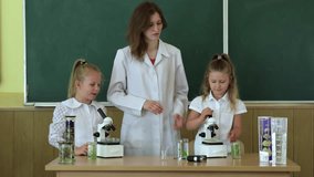 At school, a teacher and two little girls look through microscopes at a green chalkboard. Back to school. 4k video.