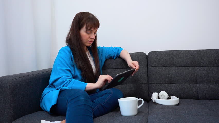 Female freelancer in blue shirt browsing the Internet using a digital tablet.