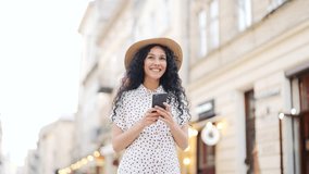 Attractive young hispanic young woman tourist in hat walking on city street using smartphone mobile phone Outdoors browsing internet, searching Technology and lifestyle travel trip and journey concept - Powered by Shutterstock - Get 15% off with code: PIKWIZARD15