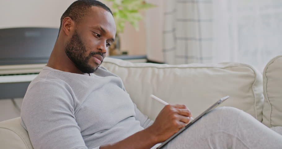 African american businessman or male writer using pen drawing, writing on tablet for online working or studing at home office. computer device for modern professional communication digital work.