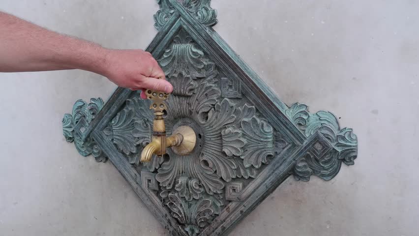 A man opens a faucet with water, the faucet of an ancient mosque in gold color, the concept of Islamic ablution, the historical mosques of Istanbul
