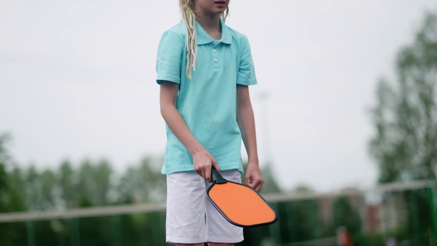 Portrait little teenage girl playing pickleball game, pickleball yellow ball with paddle in hands, outdoor sport leisure kids activity.