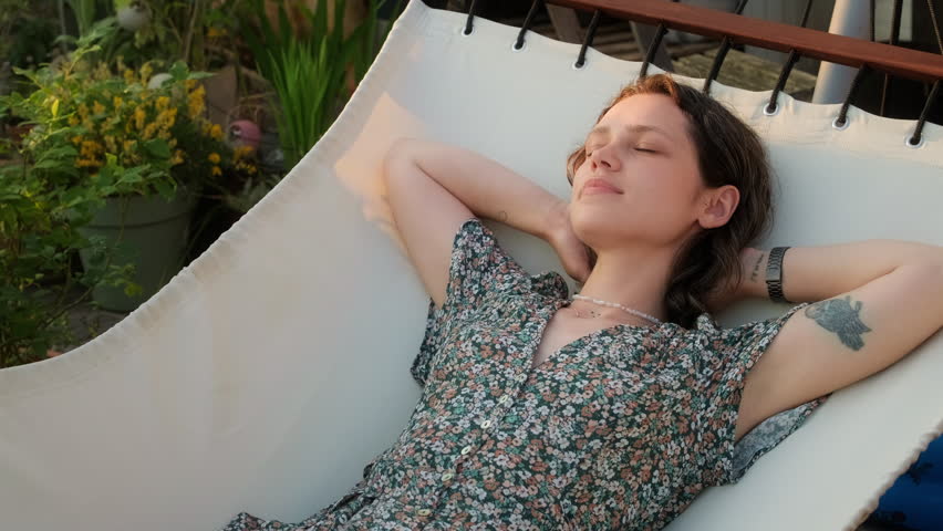 Portrait of young carefree woman enjoying a sunny day in the hammock on her terrace. Female resting stretching after work and enjoying beautiful weather sunset Royalty-Free Stock Footage #1105214193
