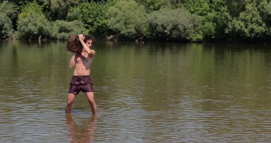 Man throwing a heavy log standing in a river, flowing water