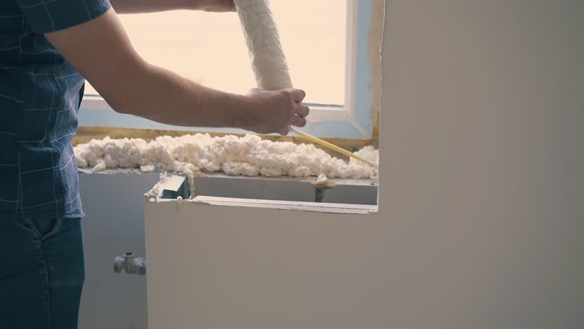 happy man in protective glasses and blue shirt applies spray foam insulation on windowsill at construction in light room Royalty-Free Stock Footage #1105221281