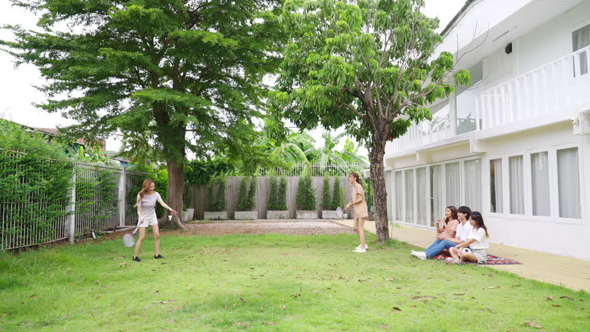 Group of Young Asian man and woman playing badminton together on backyard. Happy people friends enjoy and fun outdoor lifestyle with sport workout exercise at home together on summer holiday vacation.