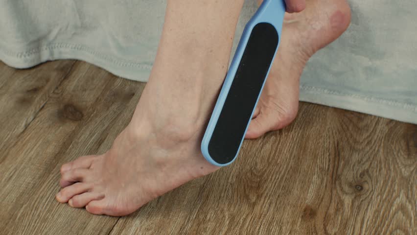 The female uses a sanding brush to exfoliate her foot. Treatment of cracked heels in women. A woman makes cosmetic procedures with a plastic grater for the skin of the heels. Callus removal concept Royalty-Free Stock Footage #1105225117