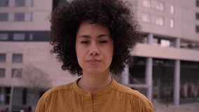 Young beautiful African American girl shakes head seriously looking at camera and afro hair. Confident and serious millennial woman posing for video. Latin people with negative expression outdoors.