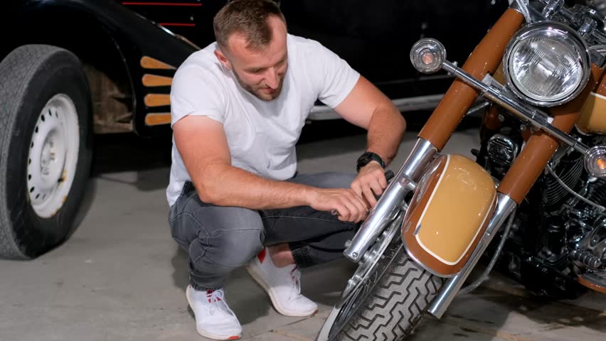 A bearded man checks the brakes on his motorcycle before going on the road. Diagnostics of a motorcycle Royalty-Free Stock Footage #1105227729