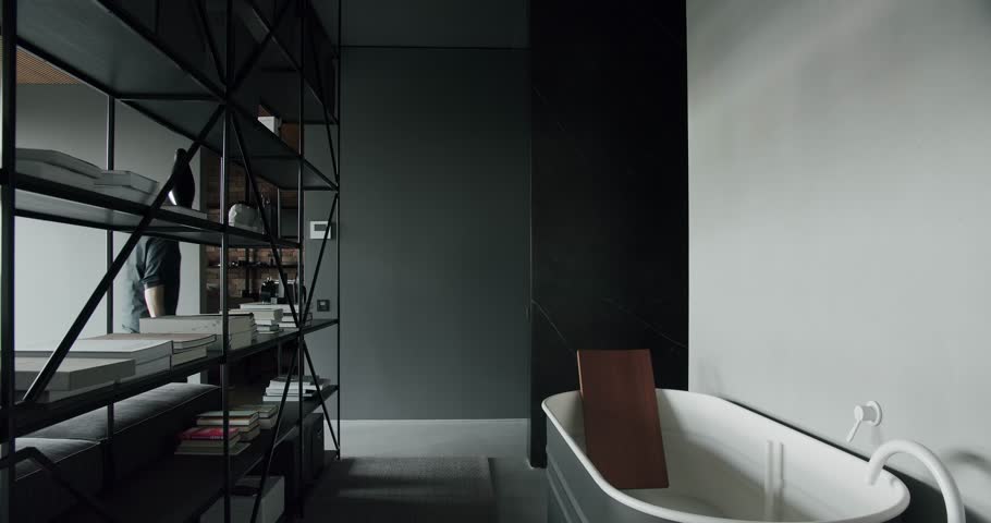 A man walking in a Luxury interior bedroom and bathroom together delimited by a modern bookshelf. minimalist modern bathtub. Luxury cozy gray Apartment. Modern bathroom with simplicity design. Royalty-Free Stock Footage #1105227887