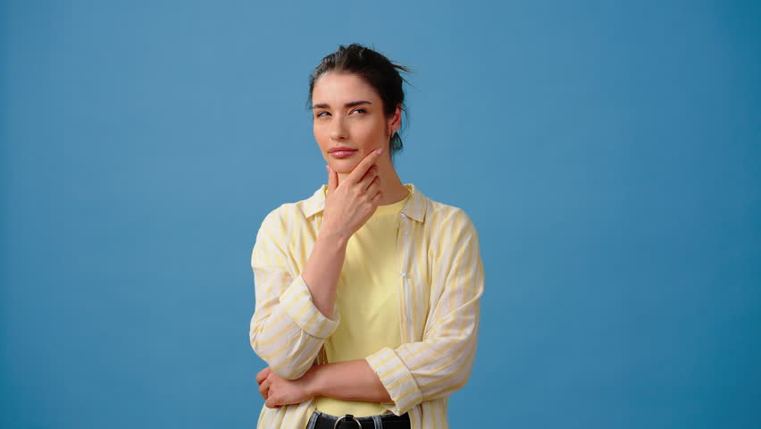 Pensive young woman massages chin thinking about solution of problem. Happy female makes eureka gesture and smiles nodding head. Person has good idea on blue background Royalty-Free Stock Footage #1105228129