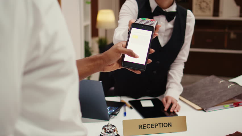 Close up of african american hotel visitor using smartphone banking app to buy holiday package deal upgrade. Receptionist using POS payment terminal to validate credit card purchase during check in Royalty-Free Stock Footage #1105231147