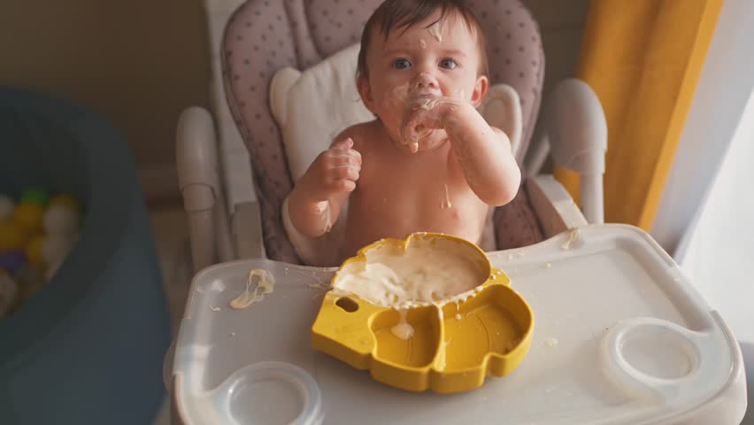 baby eats dirty. happy family kid toddler concept. baby girl dirty sitting messing with food at the table for feeding in lifestyle the kitchen. grimy toddler in the kitchen Royalty-Free Stock Footage #1105232311