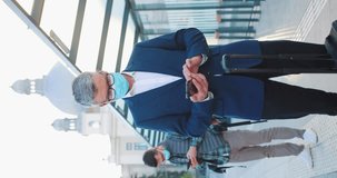 Handsome Caucasian businessman with luggage using mobile phone while waiting arrival of his transport. Man wearing face respirator during travel. Flu epidemic. COVID-19. Vertical video.
