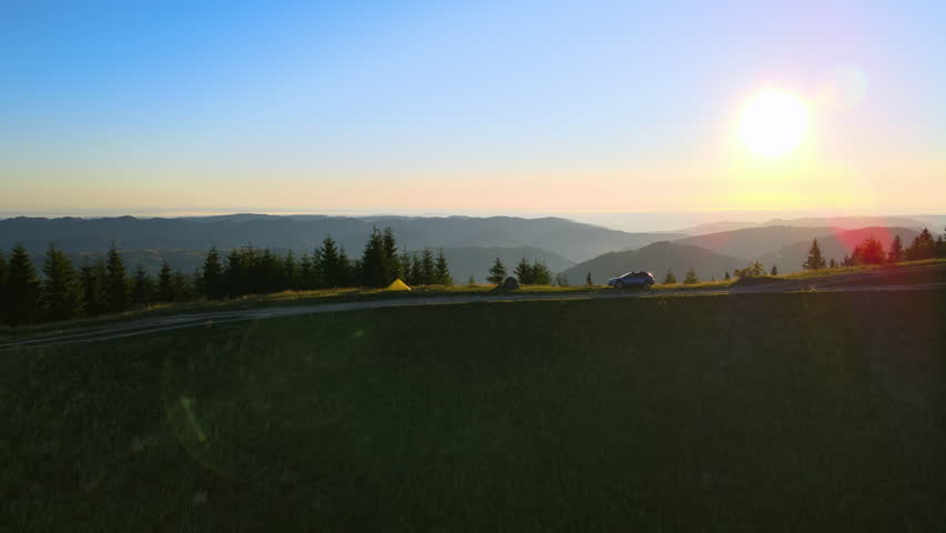 Offroad camping site on hillside at bright sunset. SUV vehicle and tent shelters on mountain campsite on sunny evening. Active tourism and hiking concept