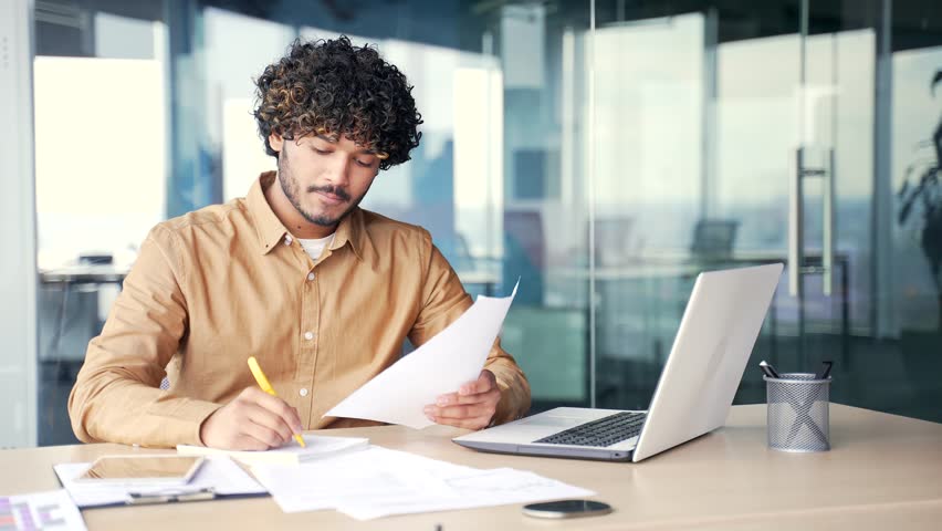 Busy young manager preparing for presentation while sitting at the desk at workplace in modern office. A positive financier checks documents, does paper work. Businessman working on startup or project Royalty-Free Stock Footage #1105252421