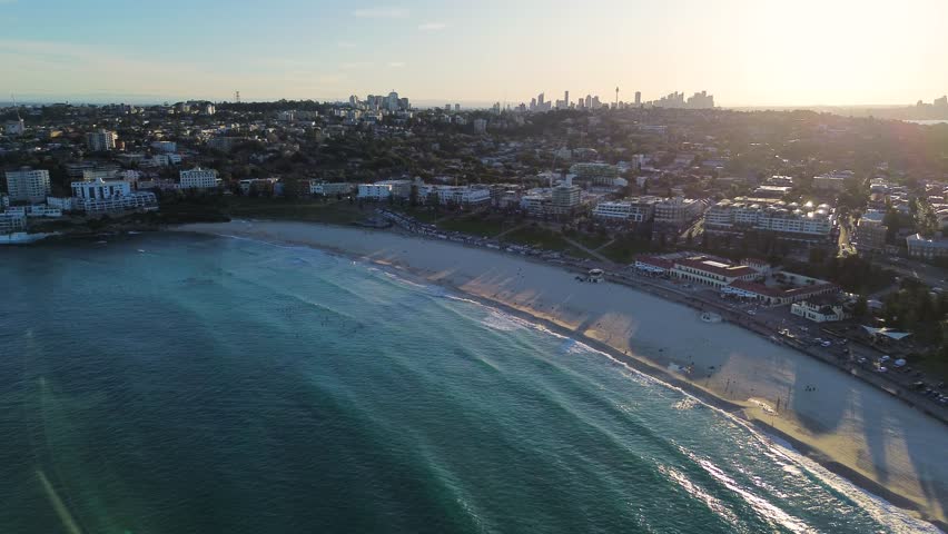 Aerial drone pan landscape scenic shot of Bondi beach ocean swell sea with Sydney City CBD in background sunset travel tourism NSW Australia 4K Royalty-Free Stock Footage #1105257129