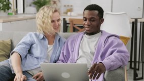 Happy young multiracial couple planning budget, working remotely, refund or mortgage approval, smiling woman and man looking at laptop screen, checking finances, sitting home together.