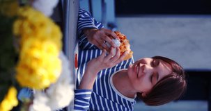 Teenager girl eating cheeseburger at sidewalk cafe. Slow motion 4k footage. Vertical video.