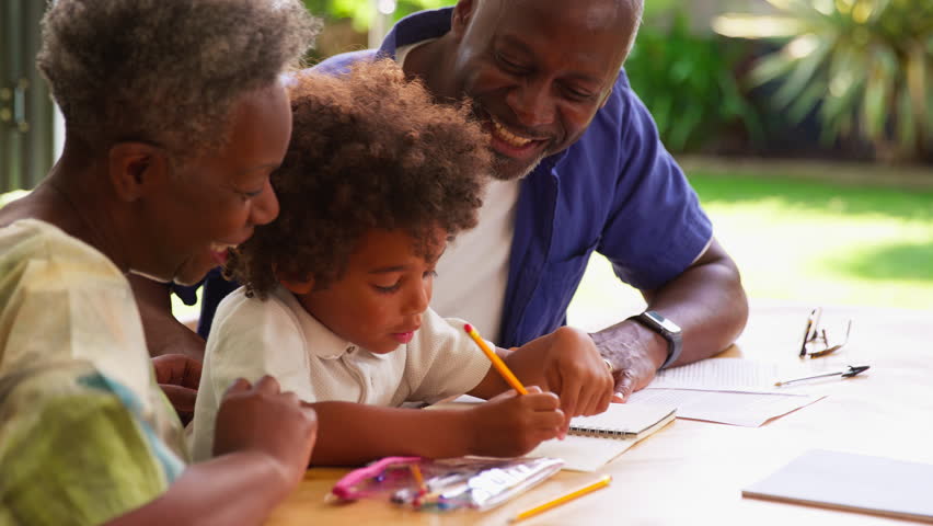 Multi-generation family with grandparents helping grandson with homework at home sitting around table - shot in slow motion