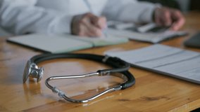 Video screensaver on medical topics. The unrecognizable face of a doctor who works at a desk, writes documents. There is a stethoscope on the table of a medical worker. Close-up. High quality 4k