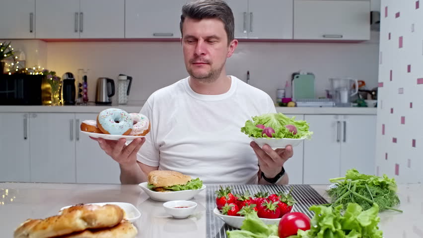 Young man making choice between healthy food and fast food. Choosing healthy meal instead of burger and doughnuts. Diet or healthy lifestyle concept. Sugar addiction