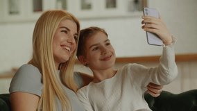 Happy young mom and sweet little daughter girl looking at webcam with toothy smile. Mother and kid taking self portrait picture on smartphone holding gadget in hand.