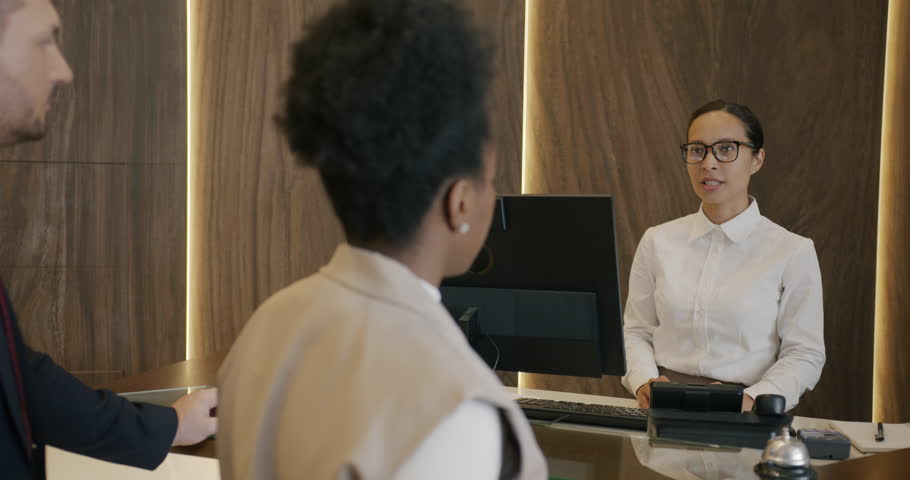 Hotel receptionist friendly young woman is talking to guests businesspeople and giving key card in lobby. Accommocation and communication concept. Royalty-Free Stock Footage #1105280581