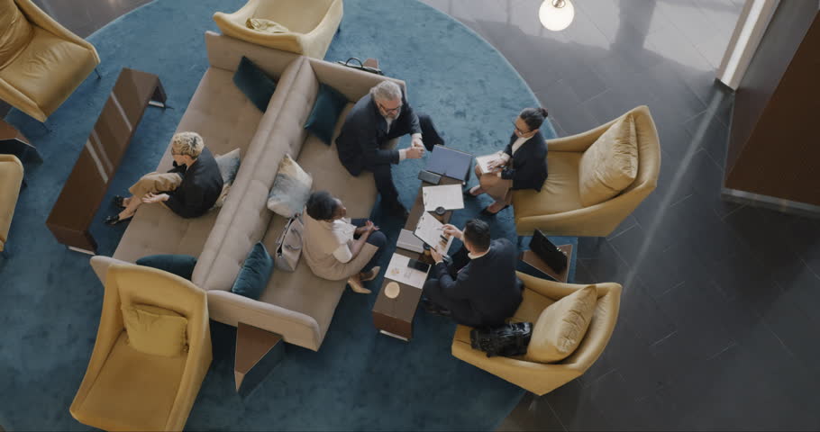 Top view of multi-ethnic business people talking at meeting in hotel lobby discussing cooperation. Occupation and travelling concept. Royalty-Free Stock Footage #1105280647