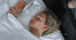 Vertical video of top view young woman sleeping on bed lying on pillow and covered with blanket. Resting woman turns while sleeping at home on bed in bedroom, in the morning before waking up