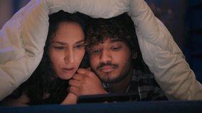 Multiracial couple Hispanic woman Indian man Arabian boyfriend girlfriend happy family under blanket cover watching movie with mobile phone talk online video call discuss internet shopping laughing - Powered by Shutterstock - Get 15% off with code: PIKWIZARD15