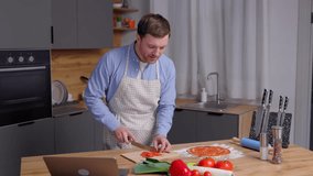 Young handsome man is preparing pizza and salad in the kitchen. The man enjoys the process of cooking.