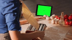 Young woman using a tablet PC in the kitchen. A woman preparing homemade italian traditional pasta using pasta machine. Green screen for chroma keying