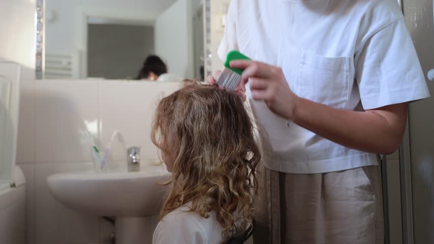 A woman helps to get rid of lice and parasites on the head of a little girl, combs her head with a special comb. Treatment of lice and nits.  | Shutterstock HD Video #1105296181