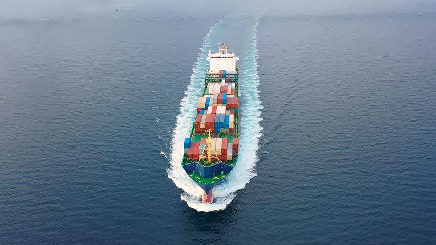 Container Ship underway full speed. Complete deck extends from bow to aft. Turquoise blue and white trails all around vessel. More water the boat can displace, bigger resulting wakes trail behind it
 Royalty-Free Stock Footage #1105297019
